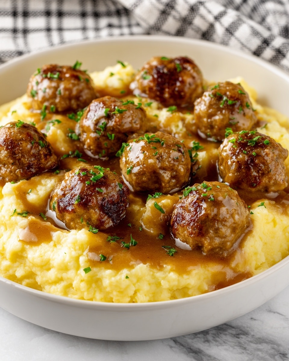 The dish shows a white bowl filled with creamy mashed potatoes as the base layer, soft and light yellow in color. There are ten round, browned meatballs placed evenly on top of the mashed potatoes, each with a slightly shiny, glazed texture. A rich brown gravy is poured over the meatballs and mashed potatoes, giving a glossy finish. The dish is sprinkled with finely chopped green herbs, adding a fresh contrast on top. The bowl rests on a white marbled surface with a blurred checkered cloth in the background. Photo taken with an iphone --ar 4:5 --v 7