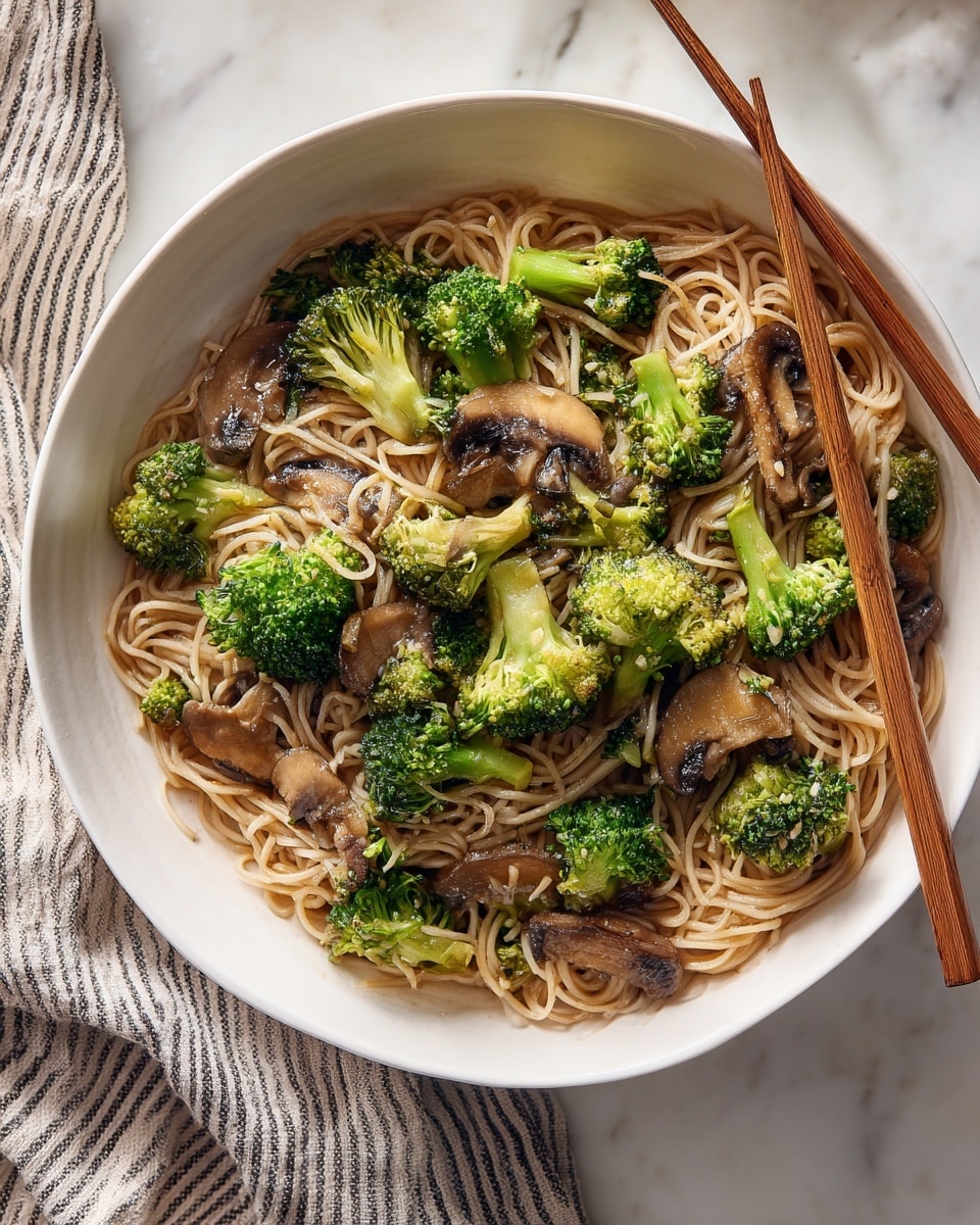 The image shows a white bowl filled with noodles mixed with pieces of cooked broccoli and slices of brown mushroom. The noodles are light brown and soft-looking, forming the base layer. On top, bright green broccoli florets are scattered evenly, adding a pop of color and texture. The mushrooms are thinly sliced and spread throughout the dish, showing a slightly shiny surface. Two wooden chopsticks rest on the edge of the bowl, pointing diagonally toward the top right corner. The bowl sits on a white marbled surface with a striped cloth visible in the top left background. The lighting is natural and soft, highlighting the textures clearly. Photo taken with an iphone --ar 4:5 --v 7
