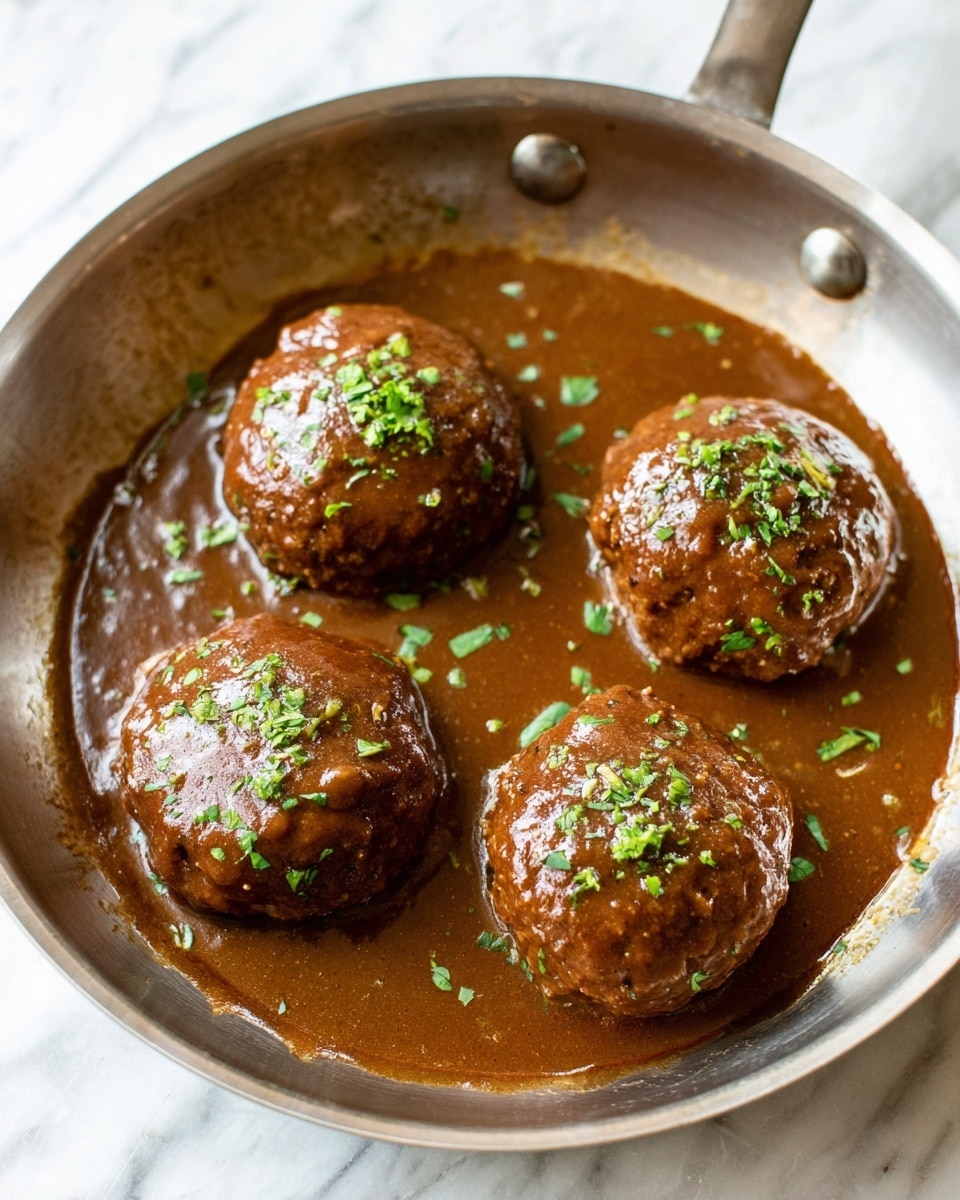 The image shows four round meat patties covered in thick brown sauce inside a metal pan. Each patty is fully coated by the sauce, which has a shiny, smooth texture. Small green herb pieces are sprinkled lightly over the top of the patties, adding a touch of color. The surface beneath the pan is a white marbled texture. photo taken with an iphone --ar 4:5 --v 7