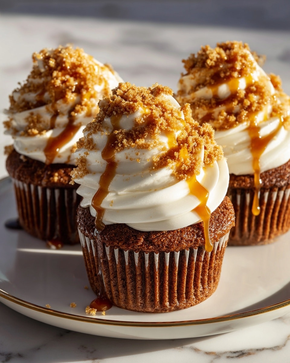 Three dark brown cupcakes with a moist texture are lined up on a white plate with a thin gold rim, placed on a white marbled surface. Each cupcake has two visible layers: a thick swirl of smooth, white cream frosting on top, and crunchy golden brown crumble pieces sprinkled over the frosting. Rich amber caramel sauce drips down from the crumble and frosting, adding shine and contrast. The sunlight highlights the textures and colors, making the cupcakes look fresh and tasty. Photo taken with an iphone --ar 4:5 --v 7