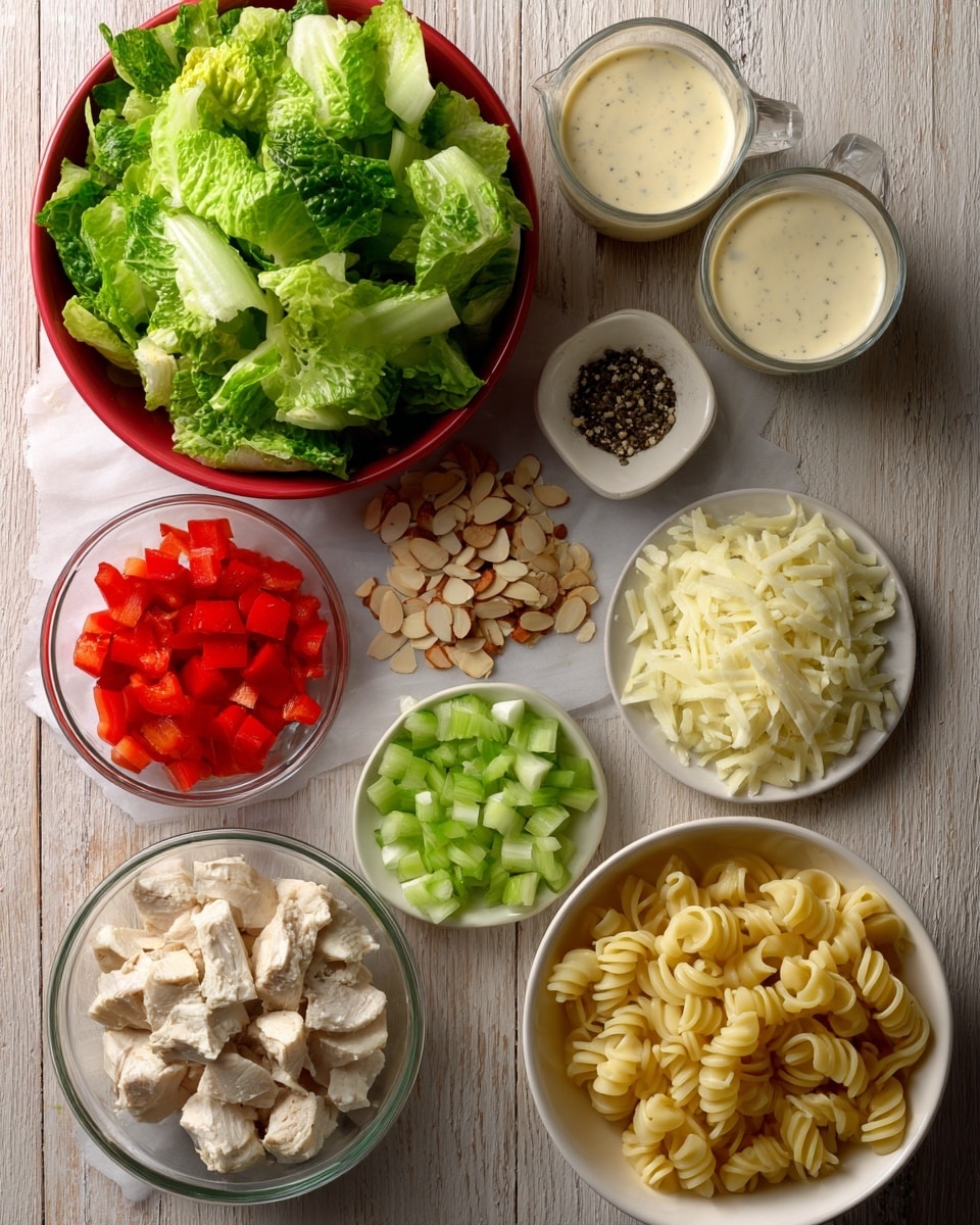 A top view of various salad and pasta ingredients arranged on white parchment paper over a wooden table. In the top left, there is a red bowl filled with chopped green romaine lettuce with a textured leafy look. Below it, loose small piles of toasted almond slices in light brown, black pepper specks, pale shaved parmesan slices, diced red bell pepper, chopped pale green celery, and finely chopped white onion are scattered. Above these piles are two light beige measuring cups filled with creamy caesar dressing and thick mayonnaise. To the bottom left, a clear glass measuring cup holds chunks of white chicken. On the bottom right, a white bowl contains curly cellentani pasta in a pale yellow color. The overall layout is neat, colorful, and fresh-looking. Photo taken with an iphone --ar 4:5 --v 7