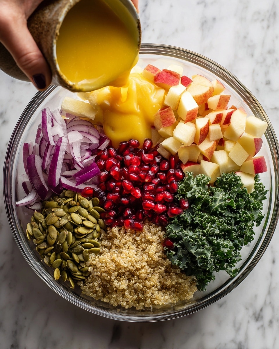 The image shows a clear glass bowl filled with several fresh ingredients separated into sections. Starting from the top left, a woman's hand is pouring a yellow-orange dressing over the bowl. Inside the bowl, there are light brown diced apples, thin purple onion slices, bright red pomegranate seeds, dark green chopped kale, fluffy light beige quinoa, and green pumpkin seeds. The background is a white marbled surface. The photo is taken with an iphone --ar 4:5 --v 7