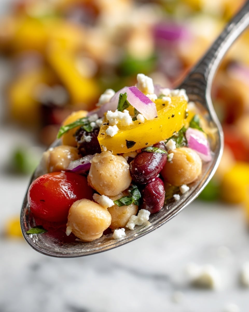 A close-up of a spoonful of a colorful salad with five main visible layers: the bottom layer has creamy beige chickpeas, the next layer features dark red kidney beans, followed by layers of bright yellow bell pepper slices and light purple onion pieces, and the top layer has fresh green herb bits along with small bits of crumbly white cheese. There is a bright red cherry tomato half resting beside the beans and other vegetables on the spoon. The background shows more of the mixed salad with similar colors and textures, all placed on a white marbled surface. photo taken with an iphone --ar 4:5 --v 7