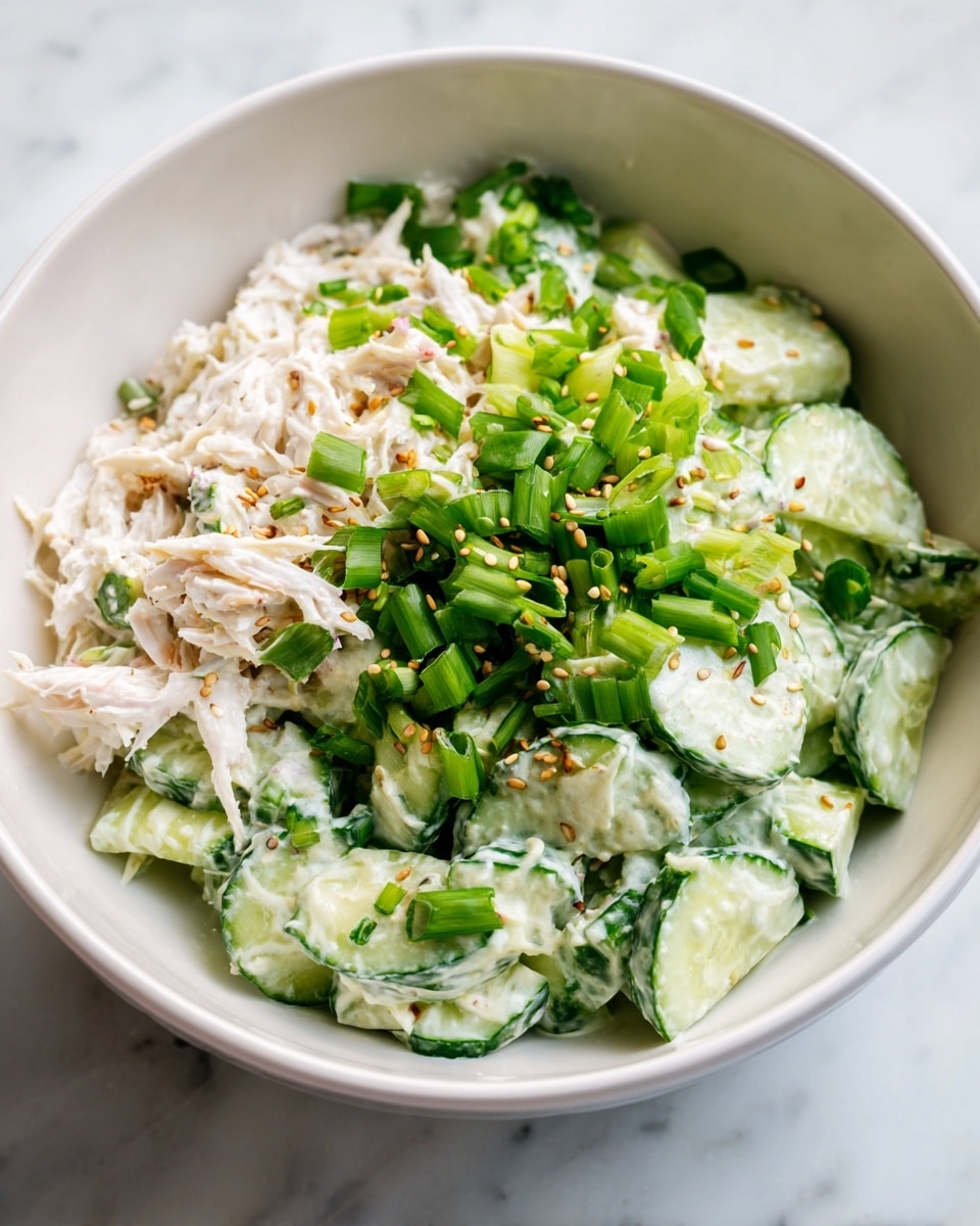 A bowl filled with a creamy salad with three main layers: the bottom layer is light green cucumber pieces with a smooth texture, the middle layer is white shredded crab meat mixed with creamy sauce, and the top layer is bright green thinly sliced scallions scattered over the salad along with small light brown sesame seeds sprinkled evenly. The bowl is white and placed on a white marbled surface photo taken with an iphone --ar 4:5 --v 7