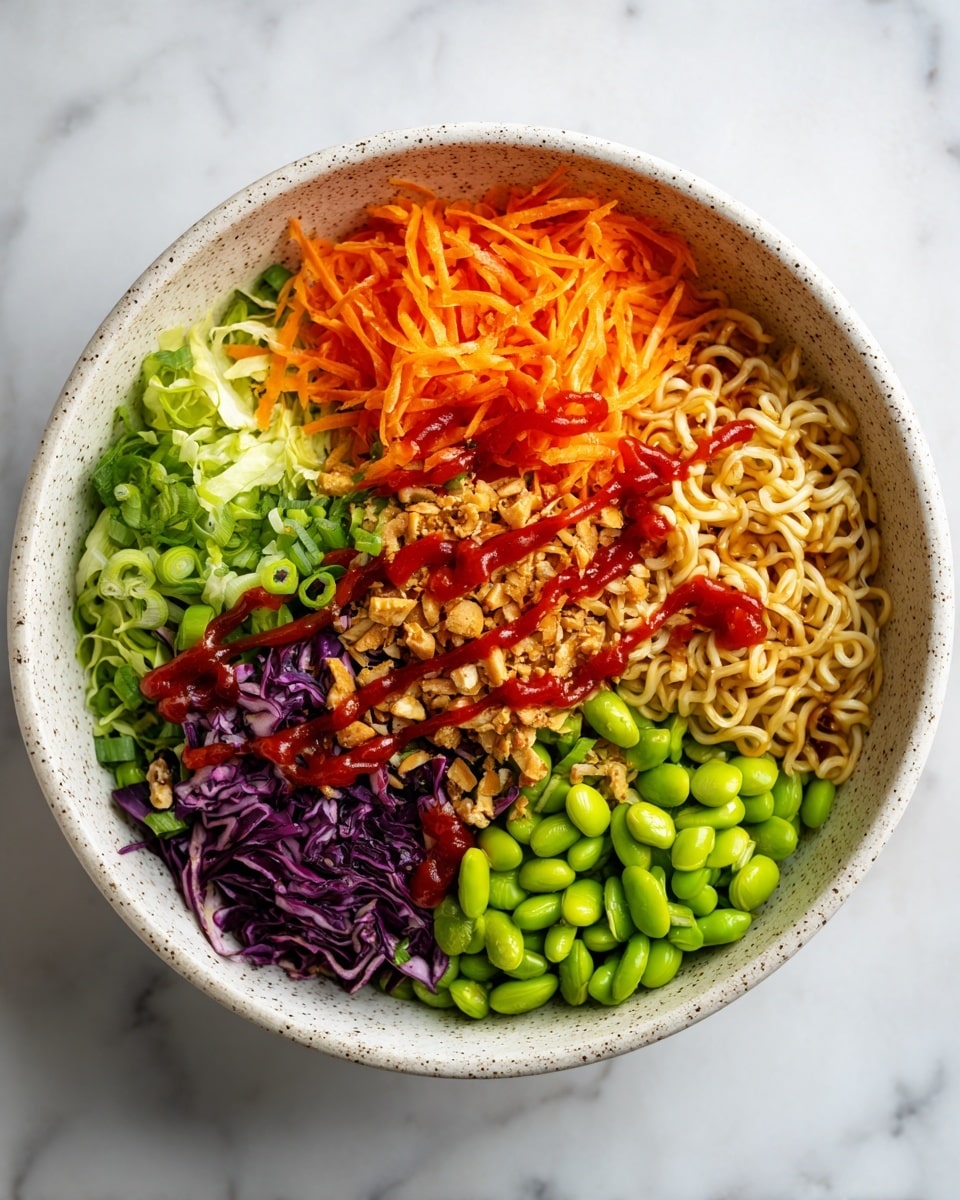 A white speckled bowl contains five main layers arranged in sections. Starting at the top left, a mound of bright orange shredded carrots sits next to a pile of light yellow-brown instant noodles mixed with small pieces of toasted nuts and sesame seeds. Below these is a mix of chopped purple cabbage and green onions, with some green lettuce layered beside it. The last section features a heap of bright green edamame beans. The entire bowl is drizzled with a thin layer of red sauce over all the ingredients, presented on a white marbled surface. Photo taken with an iphone --ar 4:5 --v 7