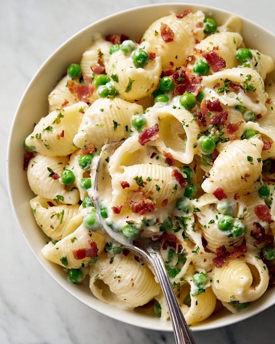 A close-up of a white bowl filled with shell pasta mixed with green peas and small pieces of crispy bacon, all coated in a creamy white sauce. The pasta shells are pale yellow with a smooth texture, and the peas are bright green, scattered evenly throughout. The bacon bits are brownish-red, adding a crunchy look. A silver spoon holds a scoop of the pasta mix, showing the creamy coating clearly and the mix of ingredients. The background surface is a white marbled texture. photo taken with an iphone --ar 4:5 --v 7