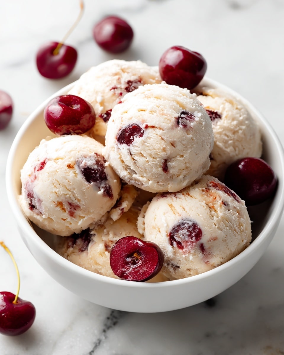 A white bowl filled with about six scoops of pale cream-colored ice cream mixed with bright red cherry swirls scattered throughout. Several whole dark red cherries sit on top and between the scoops, adding a shiny contrast. The bowl rests on a wooden surface with a blurred white marbled texture in the background. photo taken with an iphone --ar 4:5 --v 7