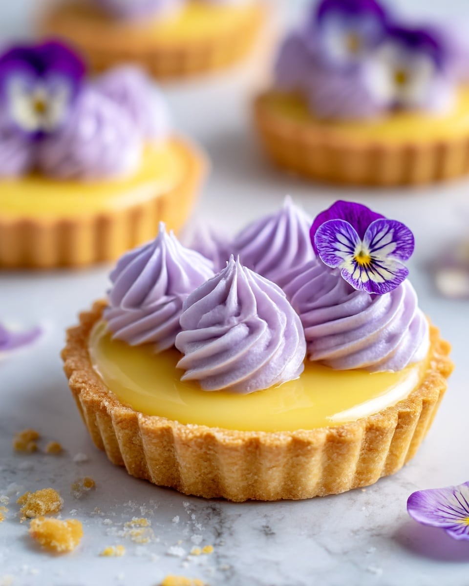 A small tart with a golden, crumbly pastry crust forms the base layer, filled with a smooth, shiny yellow custard layer. On top, there are eight swirls of light purple whipped cream arranged evenly around the tart's edge, each topped with a delicate purple edible flower with visible veins. The tart rests on a white marbled surface with a few crumbs scattered nearby. In the background, more tarts with the same decoration are slightly out of focus. photo taken with an iphone --ar 4:5 --v 7