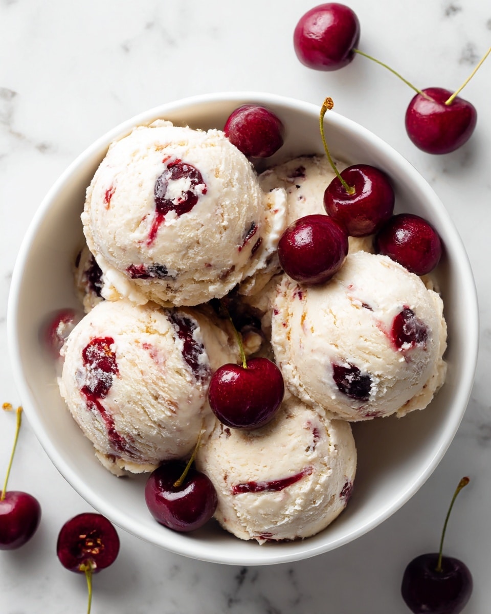 A white bowl filled with four round scoops of creamy ice cream that is pale beige with red cherry swirls and dark specks, placed on a white marbled surface. Whole dark red cherries are scattered inside the bowl around the ice cream and also outside the bowl on the surface. A silver spoon is placed inside the bowl on the right side, partially scooping one of the ice cream scoops. The ice cream looks smooth with soft creamy texture and the cherries glossy and fresh. photo taken with an iphone --ar 4:5 --v 7
