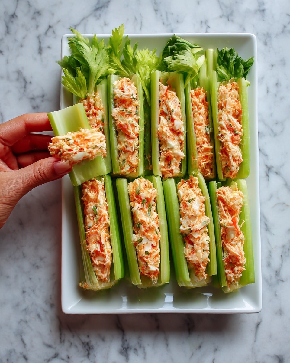 A white rectangular plate on a white marbled surface holds eleven celery sticks arranged in two rows. Each celery stick is pale green with a crisp texture and hollow groove filled generously with a creamy orange mixture with bits of light pink and white, giving it a slightly chunky appearance. A woman's hand is visible holding one celery stick. Photo taken with an iphone --ar 4:5 --v 7