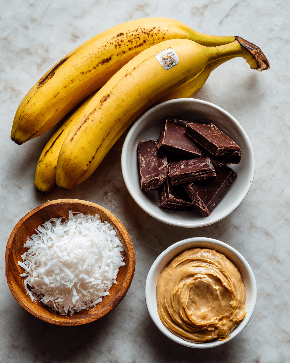 The image shows a bunch of three yellow bananas at the top center, with some brown spots and a sticker on one. Below the bananas, there is a white bowl with several dark brown pieces of dark chocolate inside. To the lower left is a small wooden bowl filled with white shredded coconut. To the lower right of the coconut bowl is a small white bowl of solid white coconut oil, shaped roughly like a teardrop. Next to the coconut oil bowl, closer to the bottom center, is a small white bowl filled with smooth, light brown peanut butter. All items are placed on a white marbled textured surface. photo taken with an iphone --ar 4:5 --v 7