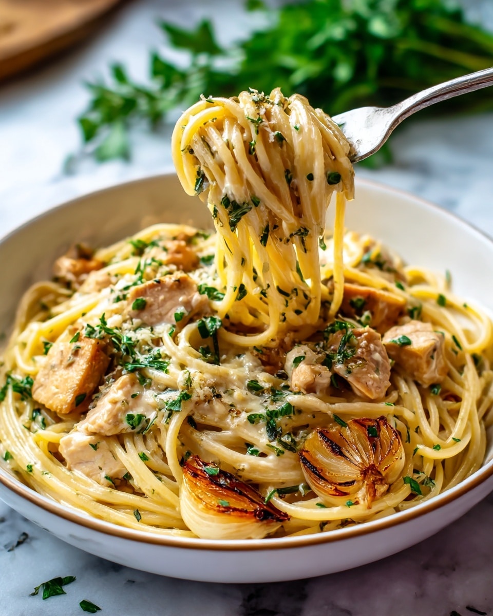 A close-up view of creamy pasta in a white bowl with two visible layers: a thick, light beige creamy sauce coating the long spaghetti noodles and small pieces of light tan cooked chicken mixed throughout. The top layer shows a fork lifting a twisted bundle of noodles, highlighting the rich sauce's smooth texture with some small green herb garnishes scattered around. A few pieces of golden brown grilled onions add contrast on the side within the noodles. The bowl sits on a white marbled surface, and a blurred green herb appears in the background. Photo taken with an iphone --ar 4:5 --v 7