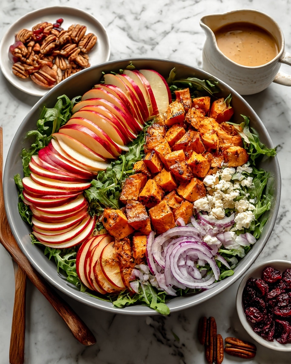 A large round bowl filled with a salad shows a base layer of green leafy vegetables. On top, there are several slices of red and yellow apples arranged in neat fan shapes on two sides. The center is covered with small, cubed pieces of roasted orange sweet potatoes with a slightly browned texture. Scattered around the bowl are thin slices of purple onion, small white chunks of cheese, and a few pecan nuts. In one corner, there is a small pile of dark dried cranberries. Two wooden salad spoons rest on the side of the bowl. The bowl sits on a white marbled surface, with a white plate holding red apples and small white dishes filled with more pecans and dressing visible nearby. Photo taken with an iphone --ar 4:5 --v 7